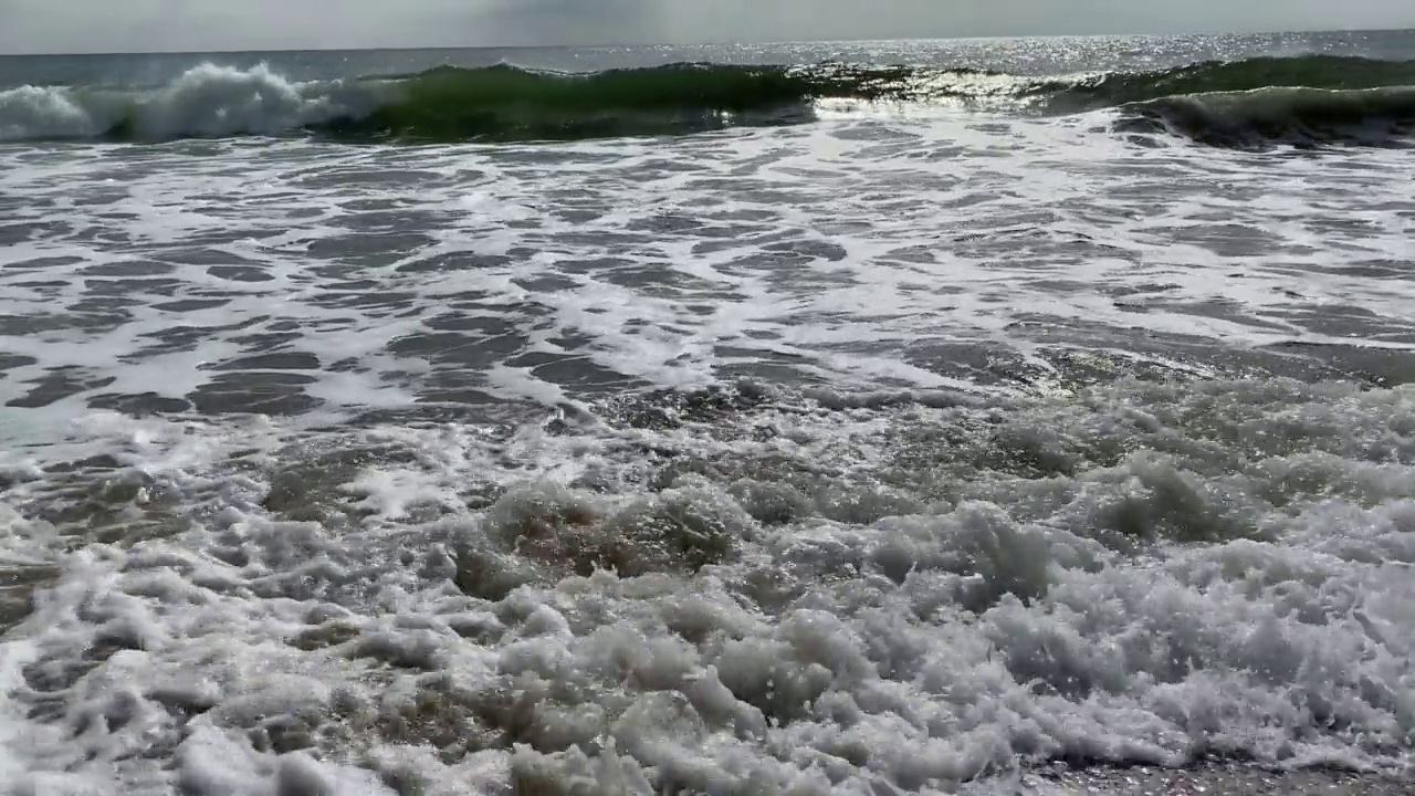 沙滩上的沙子上有海浪，海浪和黄色的沙子上有白色的泡沫，海浪覆盖着沙子视频素材