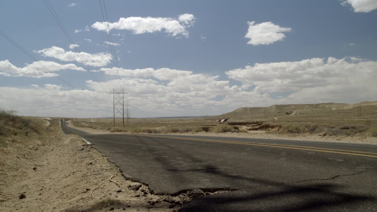 广角的乡村公路或沙漠公路穿过干燥的沙漠地区。在bg中可见电源或电话线。山区可见的山或山坡。蓝天白云。视频素材