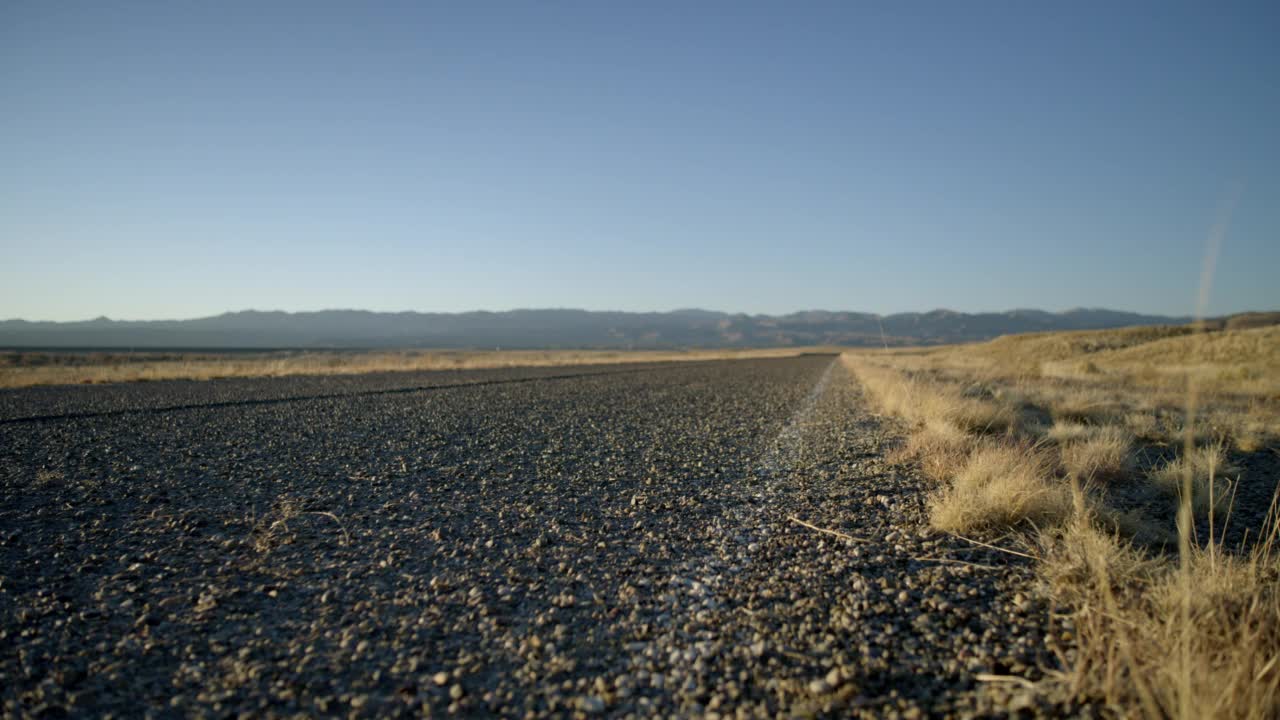 中等角度的风滚草滚过沙漠公路，公路，或高速公路从左到右。山脉可见bg。视频素材