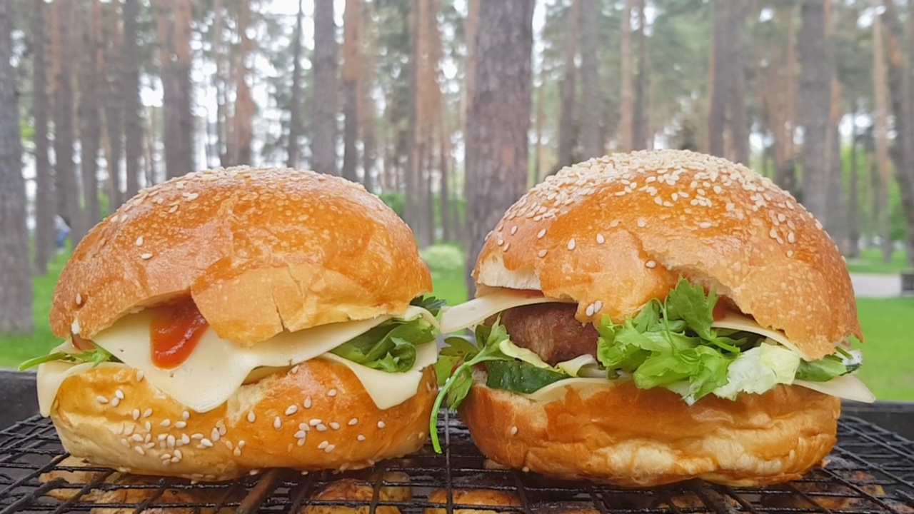 特写两个大的DIY汉堡在公园里烧烤，休息和烹饪在夏天的野餐，食物，美味，色彩鲜艳。不健康食品的概念。快餐视频素材