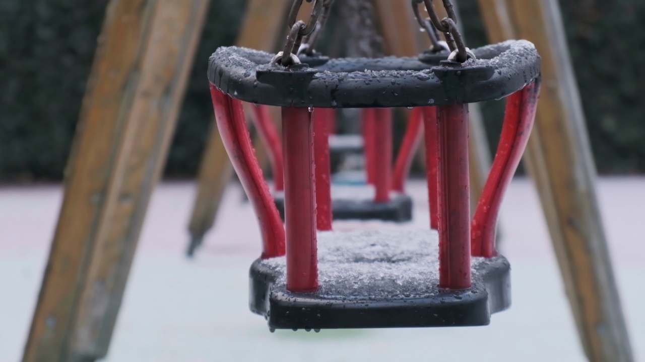 空旷的红黑相间的雪在儿童游乐场荡秋千。视频素材