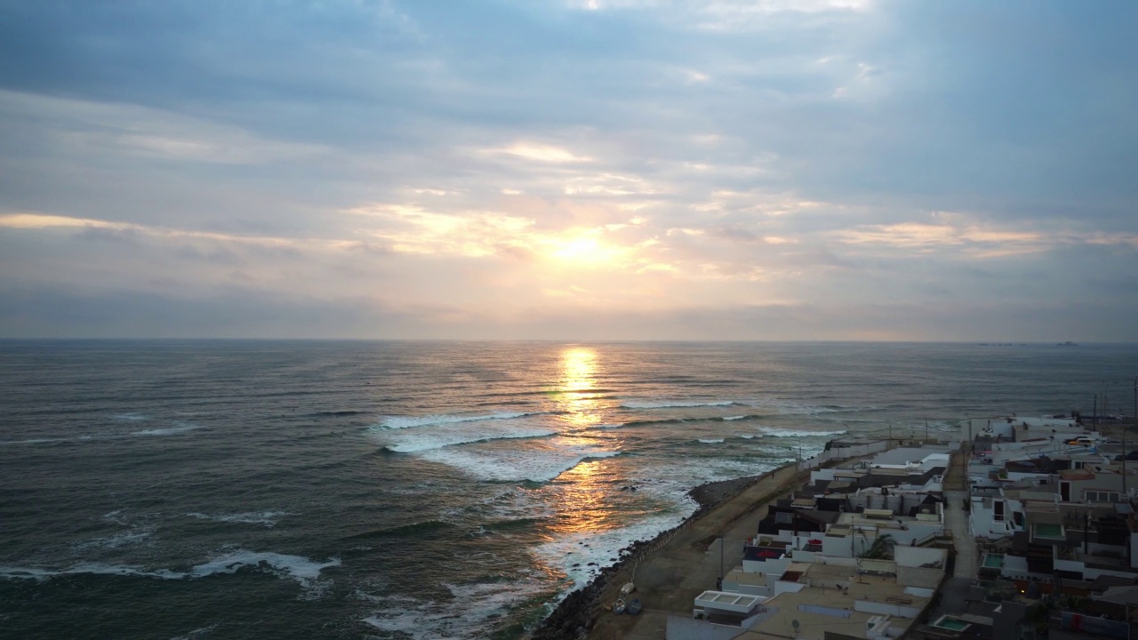 一个美丽的日落在海滩上的视频，太阳反射在水中，海浪与蓝色和紫色的天空之间的房子在4k视频素材