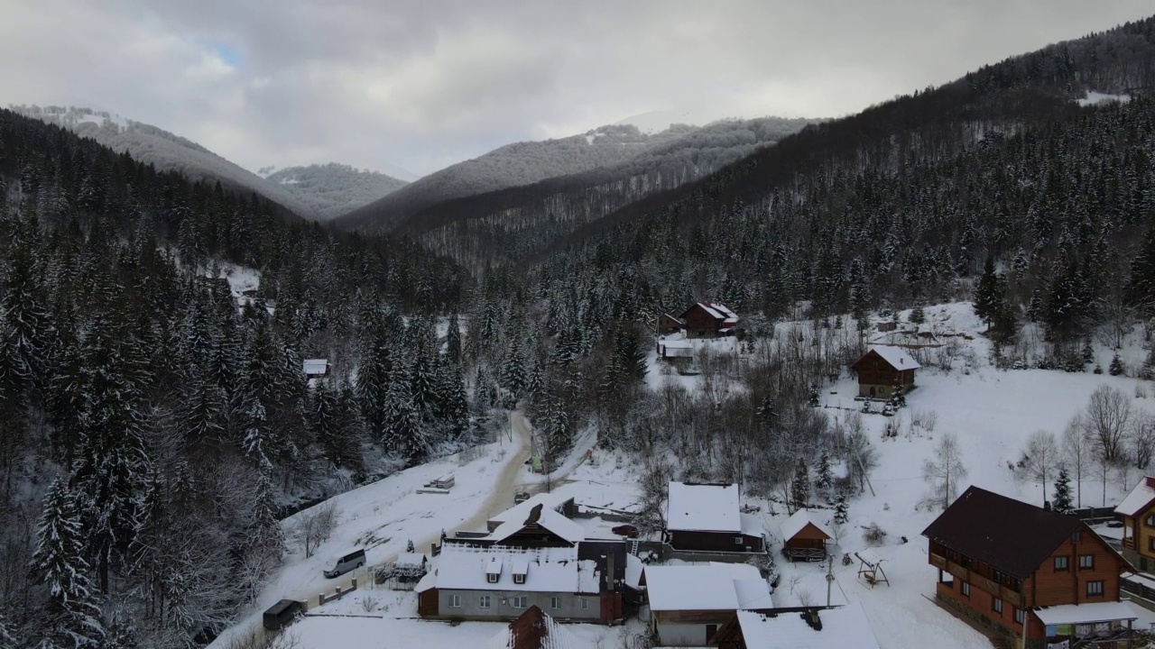 正在滑雪度假村上空飞行4K无人机。空中的冬季景观与小村庄的房子之间的积雪覆盖的森林在寒冷的山脉。视频素材