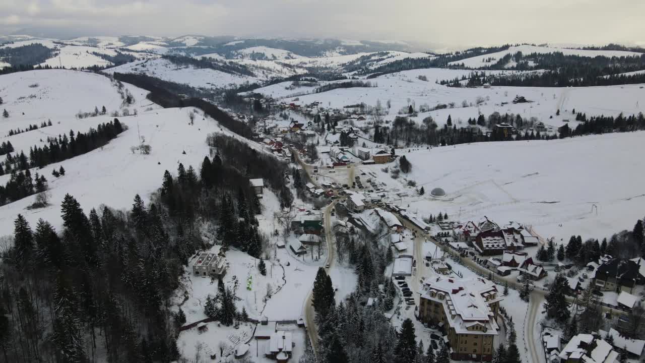 正在滑雪度假村上空飞行4K无人机。空中的冬季景观与小村庄的房子之间的积雪覆盖的森林在寒冷的山脉。视频素材