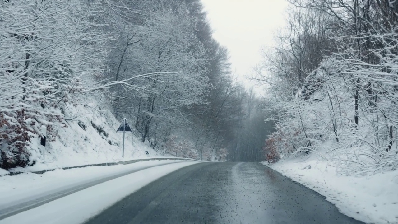 POV在大雪中行驶在有冬季树木环绕的乡村道路上，慢动作视频素材