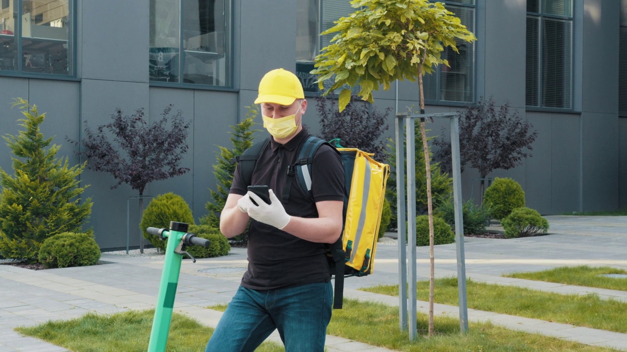 快递员戴着口罩，用手机搜索城市街道上的地址。用智能手机在户外送餐的自行车快递员。快递服务和小型企业理念视频素材