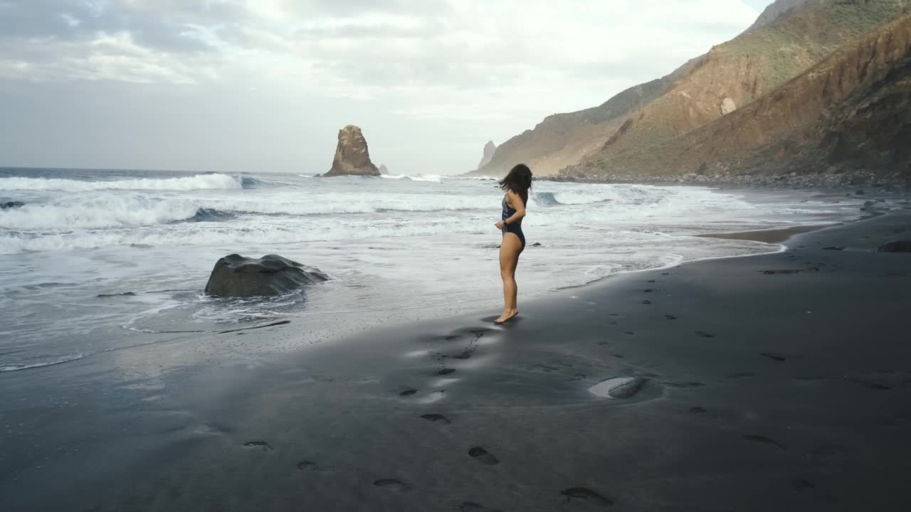 身穿泳衣的年轻女子在特内里费岛加那利岛北部的黑色火山黑色沙滩Benijo上跑步视频素材