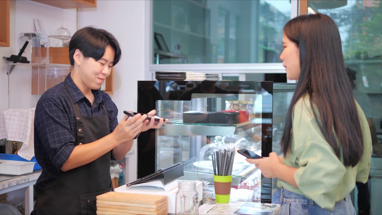 在咖啡店或餐厅，一名亚洲女性顾客和咖啡师使用智能手机扫描另一部智能手机上的QR码标签，接受数字支付。视频素材