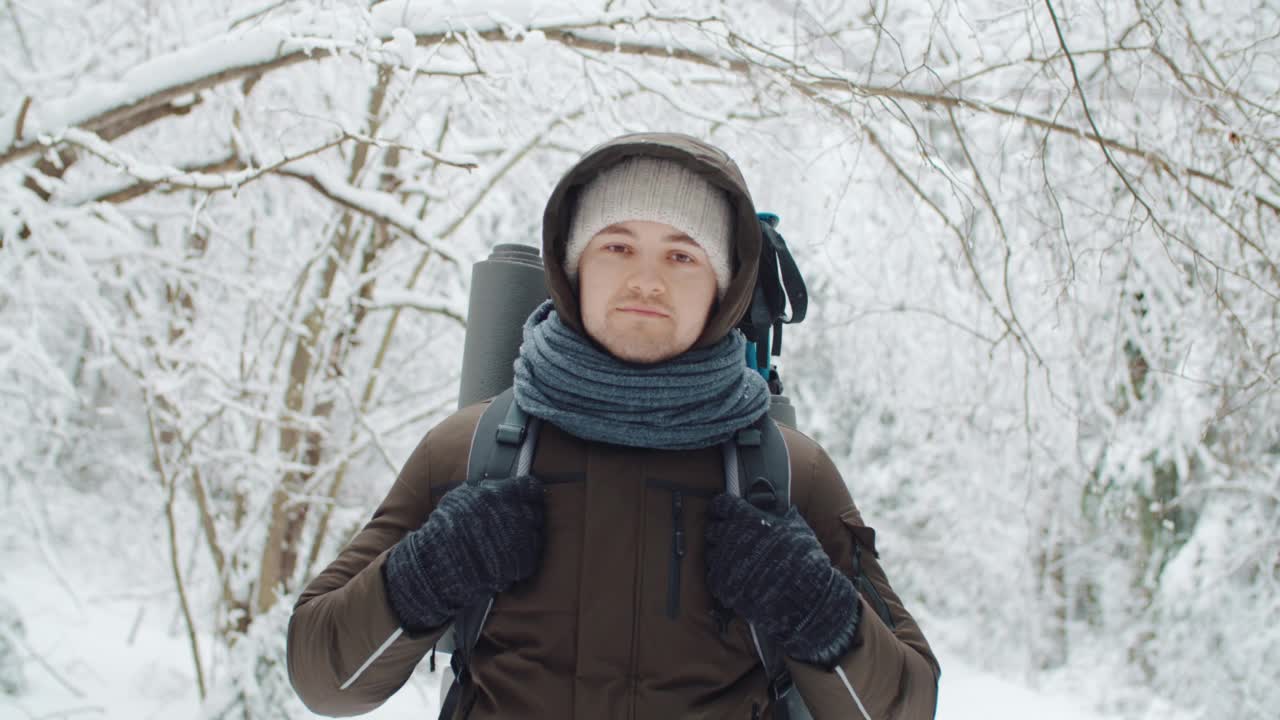 手持肖像年轻愉快的旅行者放松在冬季森林下雪。快乐的徒步旅行者看着相机，微笑着享受在白雪覆盖的树林里的徒步旅行。雪花。人与自然的概念视频素材