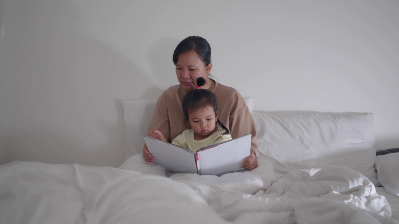 晚上，孩子和妈妈一起在床上享受着一本儿童读物视频素材