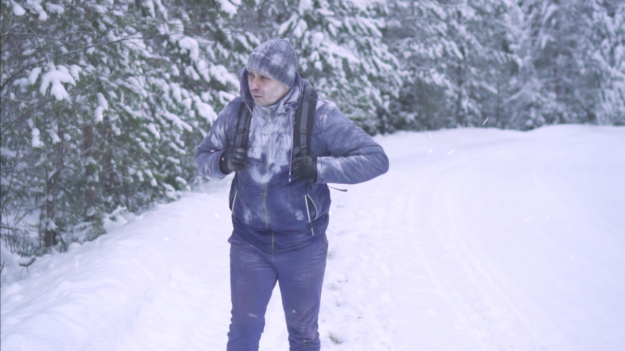 人像冻住了男人在雪地里，背着背包慢悠悠地走在树林里视频素材