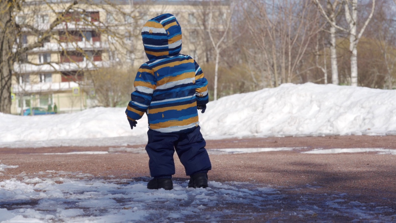 孩子在冬天的雪地里迈出第一步，1岁的小男孩在公园里学习走路。视频素材