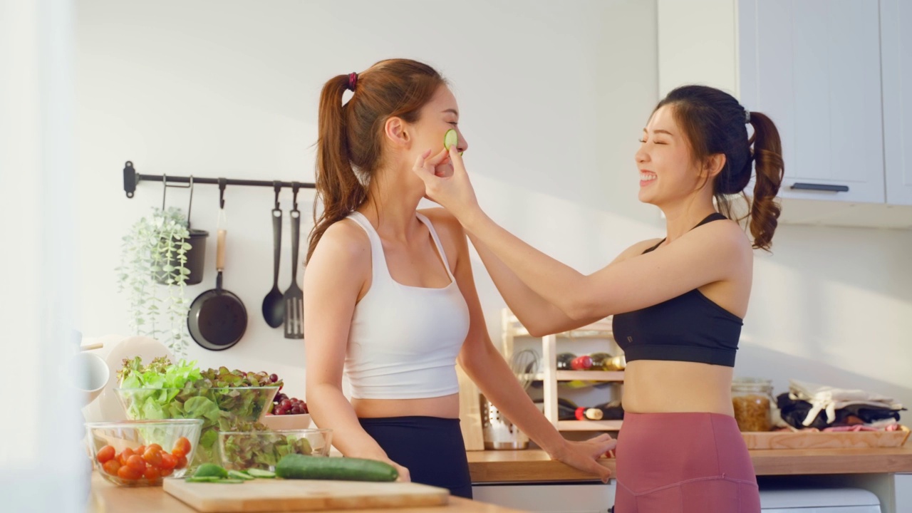 两个穿着运动服的亚洲年轻女子在厨房里做沙拉。活泼漂亮的女孩姐姐感到快乐，喜欢吃蔬菜健康的食物来减肥，在家里的保健视频素材