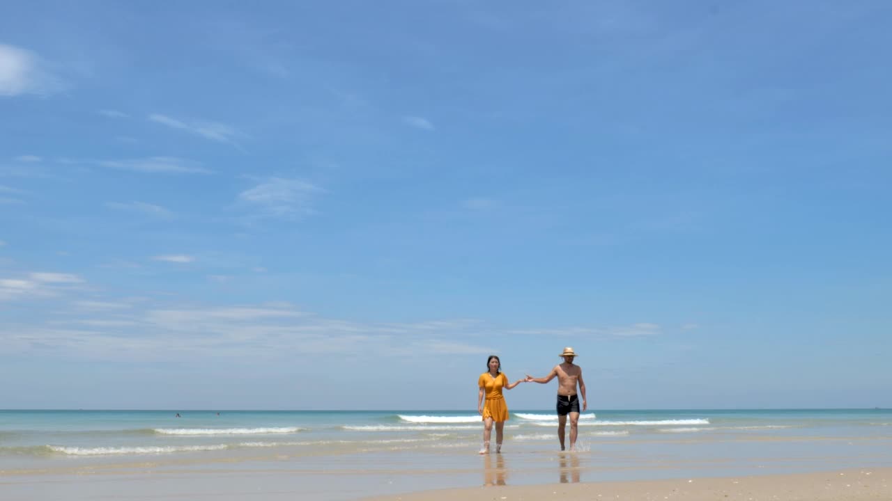 幸福的情侣相爱，在阳光明媚的海滩上玩耍，在海浪中奔跑和戏水，旅行度假的生活方式视频下载