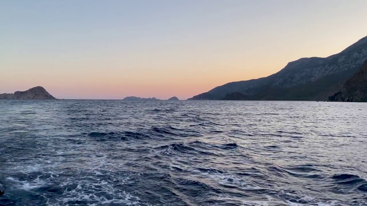 从空中俯瞰平静的深蓝色海水表面，多云的日落或日出天空和山脉的剪影。实时4k视频视频素材