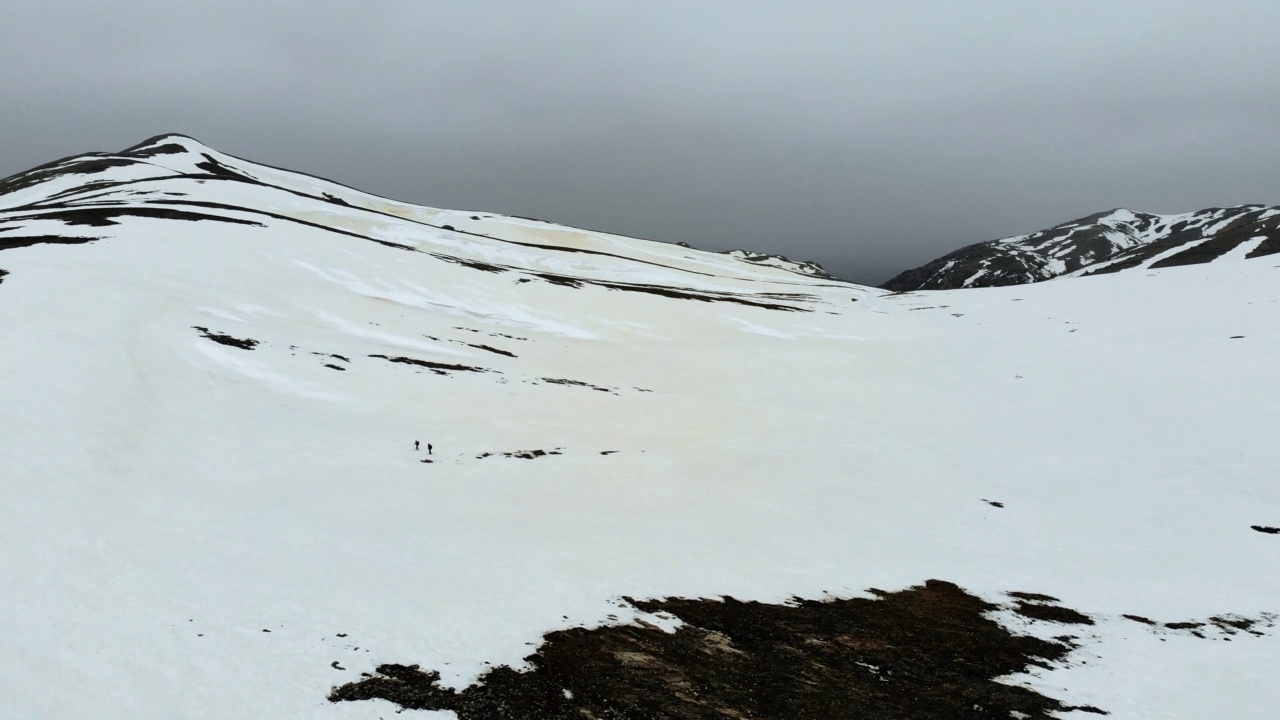 无人机拍摄的成功登山队在冬季在高海拔雪山山顶的山脊上排成一行攀登视频素材