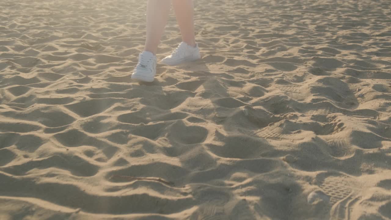 夏天，一个穿着白色运动鞋的女孩走在沙滩上视频素材