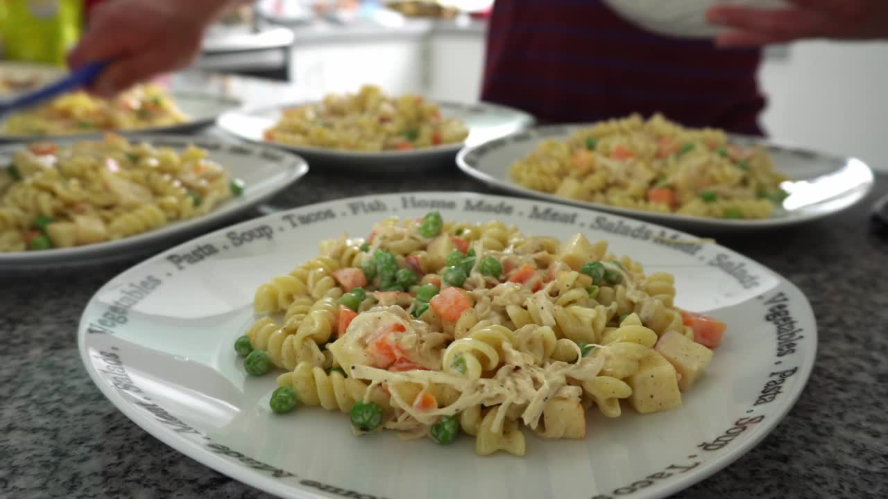 白天在厨房里几碗螺旋面沙拉，鸡肉丝，奶酪，胡萝卜片和青豆特写4k视频素材