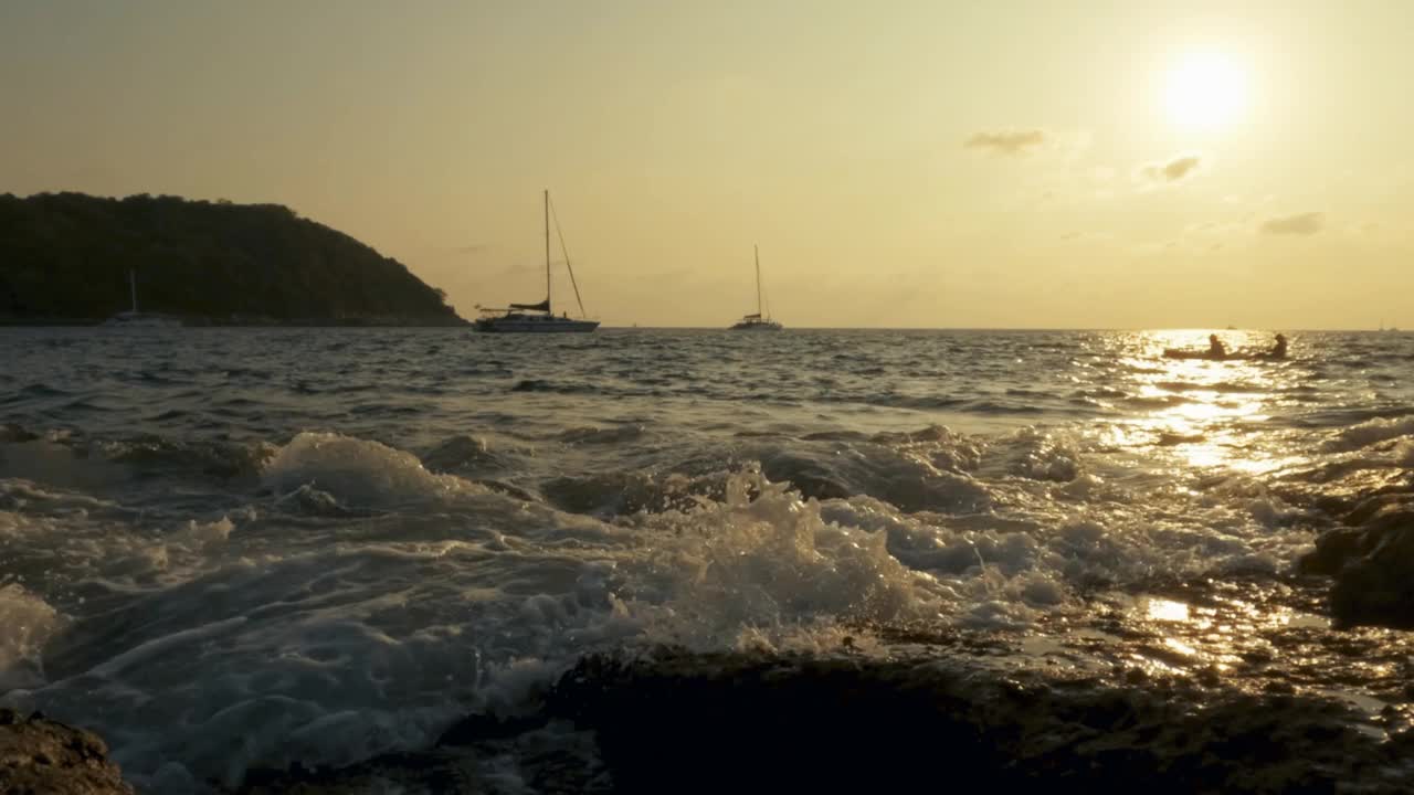 慢动作4k，有许多船载着游客看日落。两名游客划着独木舟，海浪拍打着岩石视频素材