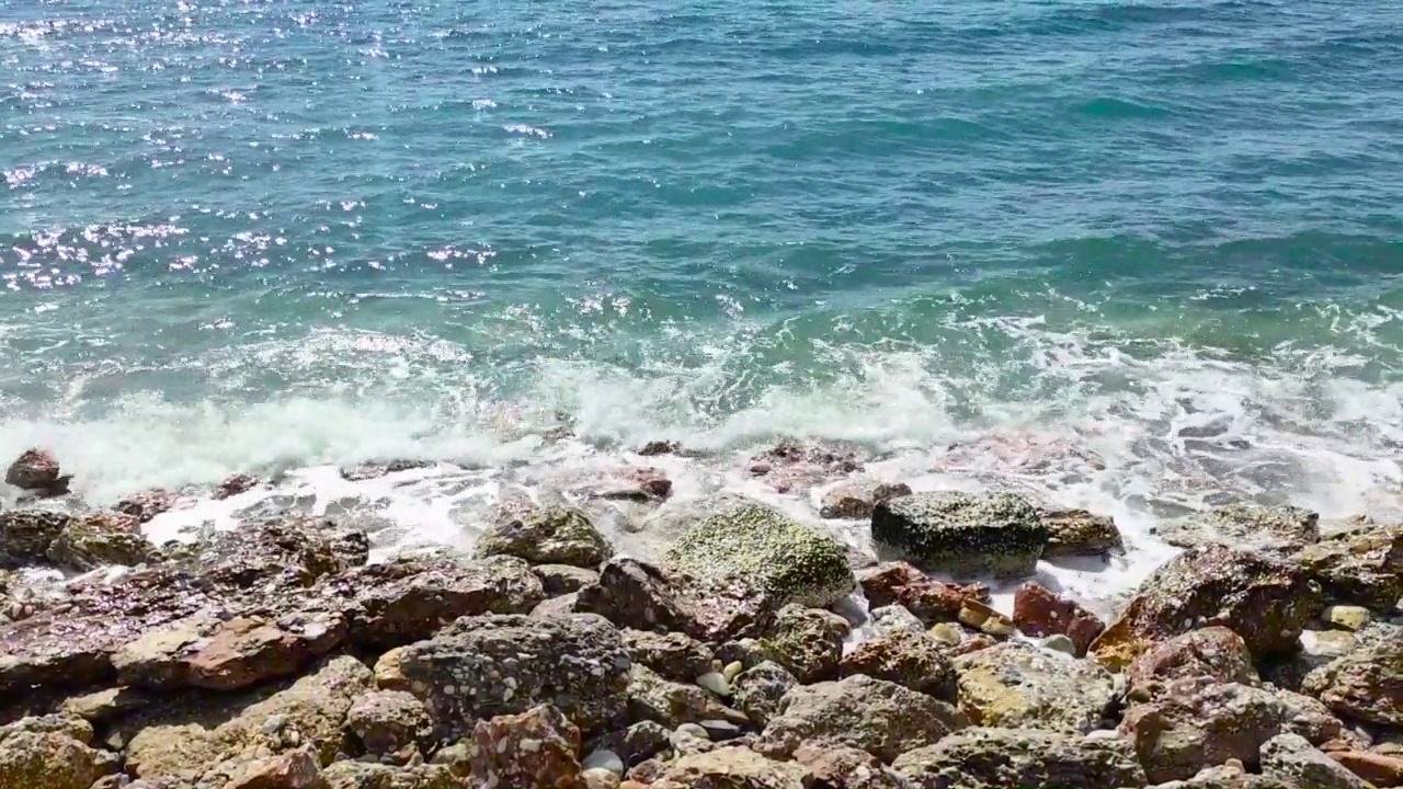 海浪拍打着海岸上的石头。蓝色的大海，淡淡的暴风雨，白色的浪花，晴朗的天气。视频素材