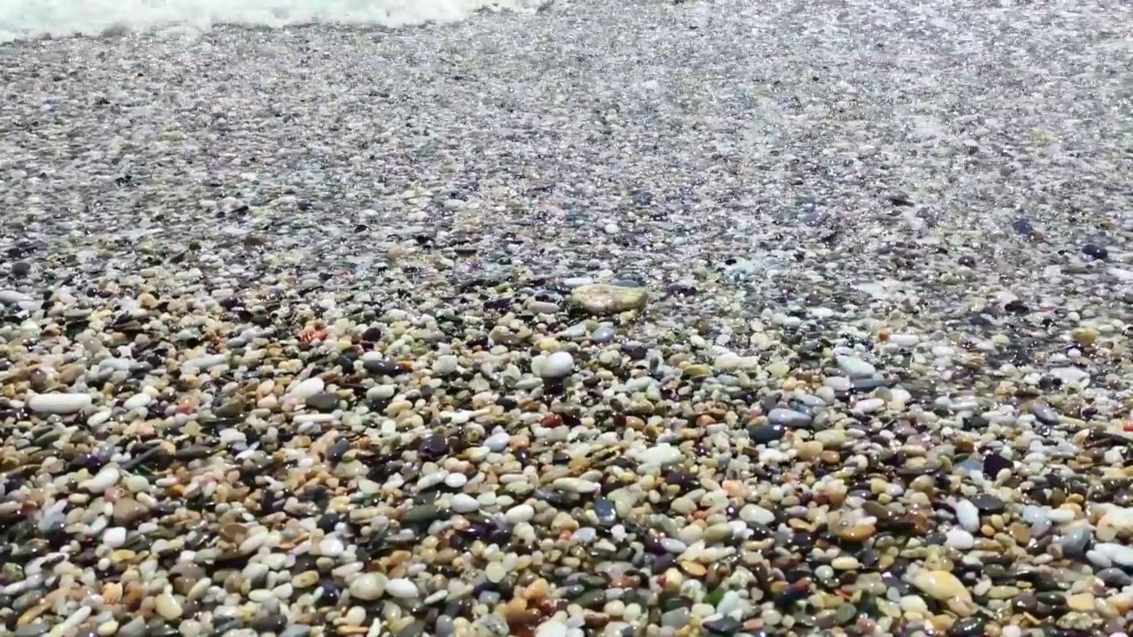 海浪拍打着海岸上的石头。蓝色的大海，淡淡的暴风雨，白色的浪花，晴朗的天气。视频素材