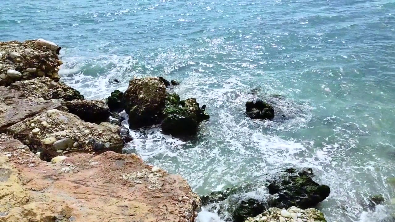 海浪拍打着海岸上的石头。蓝色的大海，淡淡的暴风雨，白色的浪花，晴朗的天气。视频素材