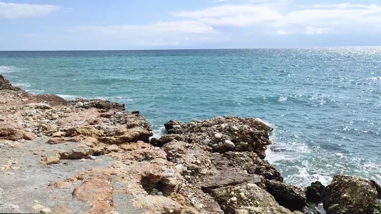 海浪拍打着海岸上的石头。蓝色的大海，淡淡的暴风雨，白色的浪花，晴朗的天气。视频下载