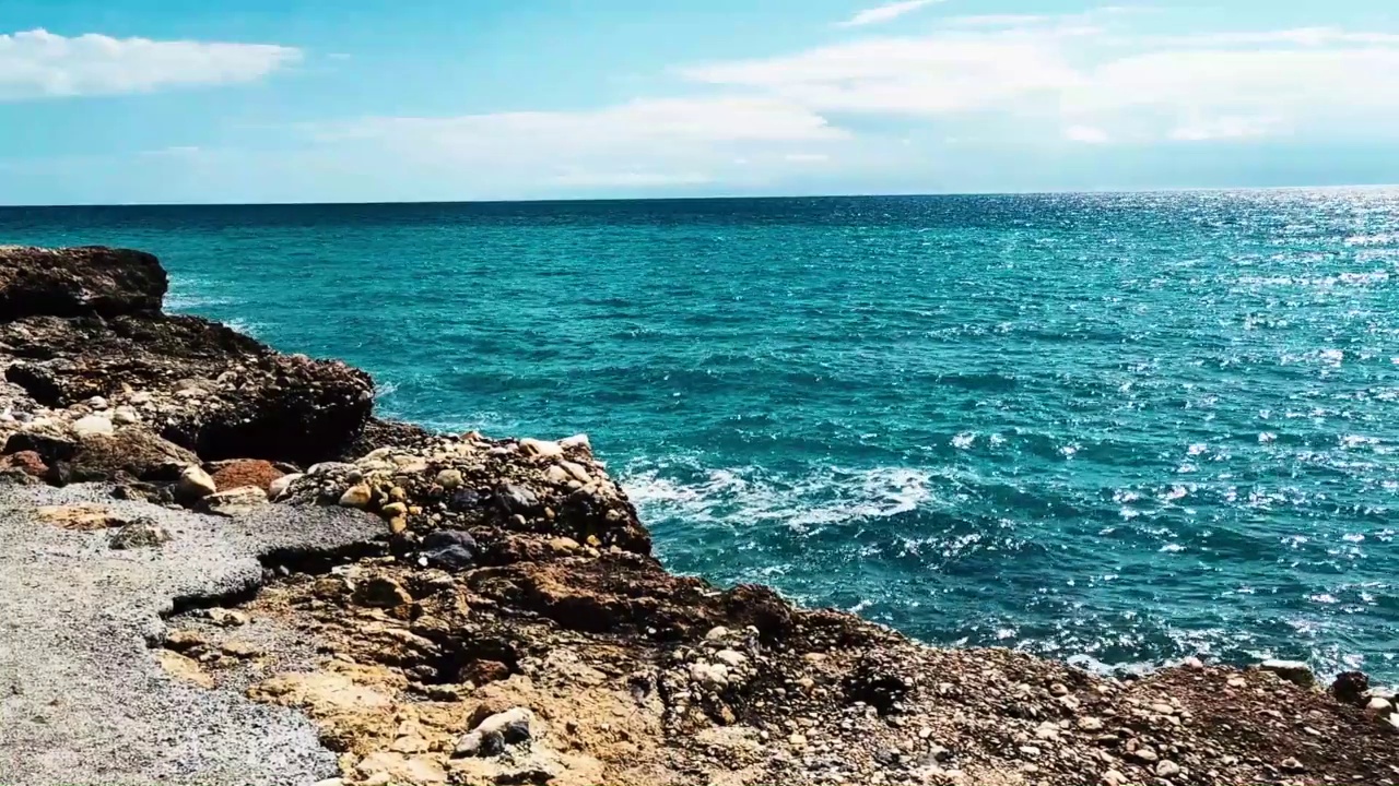 海浪拍打着海岸上的石头。蓝色的大海，淡淡的暴风雨，白色的浪花，晴朗的天气。视频下载