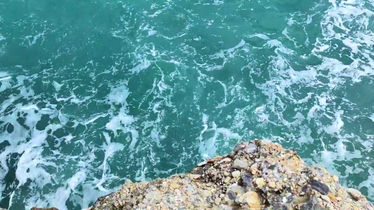 海浪拍打着海岸上的石头。蓝色的大海，淡淡的暴风雨，白色的浪花，晴朗的天气。视频素材