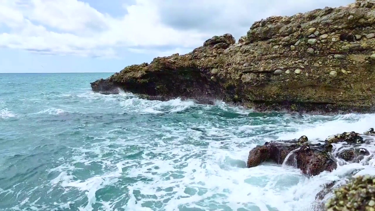 海浪拍打着海岸上的石头。蓝色的大海，淡淡的暴风雨，白色的浪花，晴朗的天气。视频素材