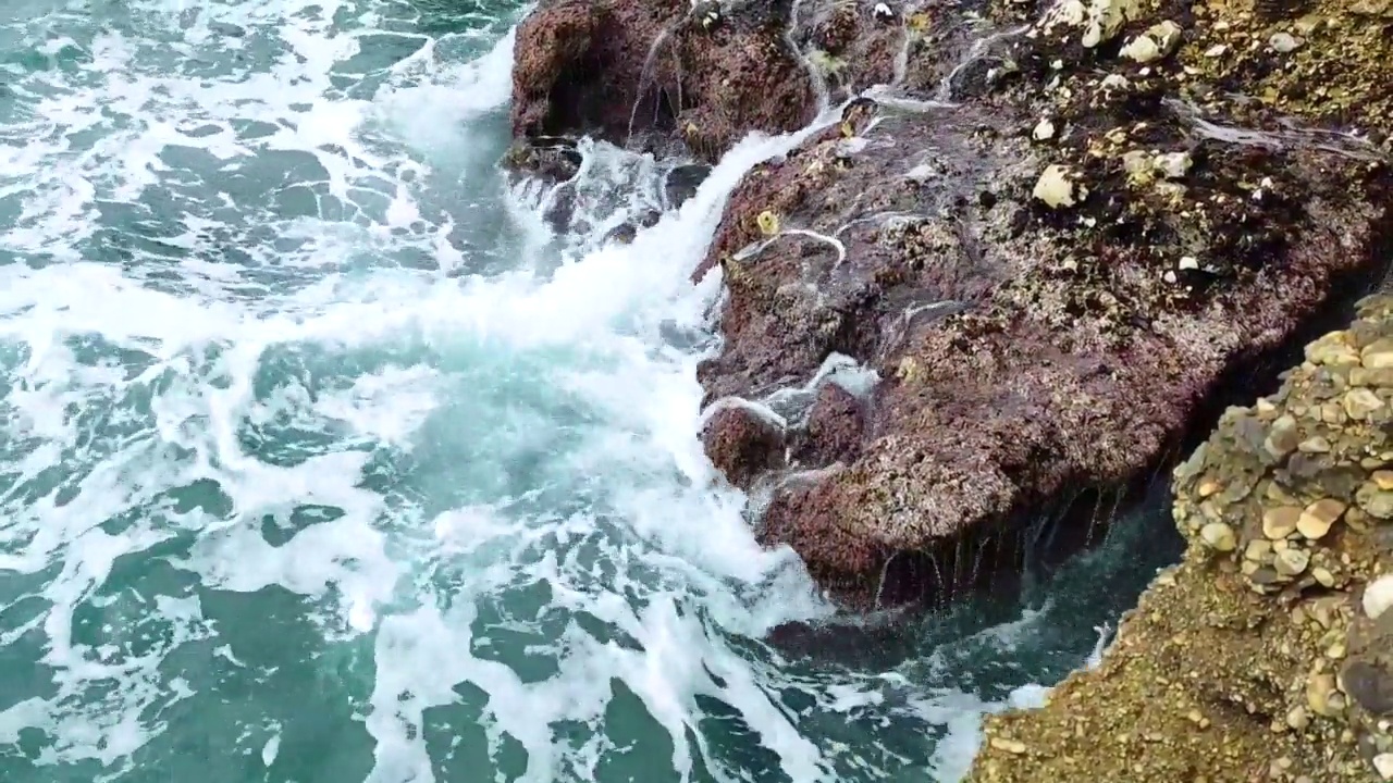 海浪拍打着海岸上的石头。蓝色的大海，淡淡的暴风雨，白色的浪花，晴朗的天气。视频素材