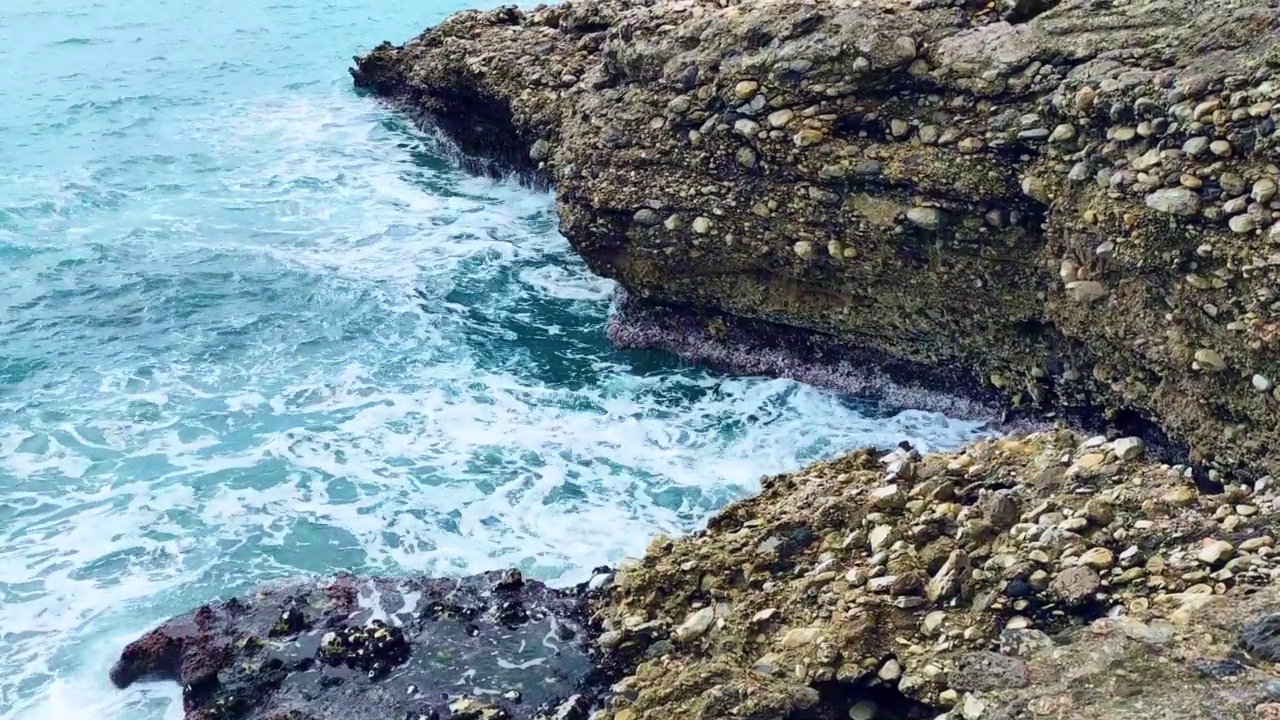 海浪拍打着海岸上的石头。蓝色的大海，淡淡的暴风雨，白色的浪花，晴朗的天气。视频下载