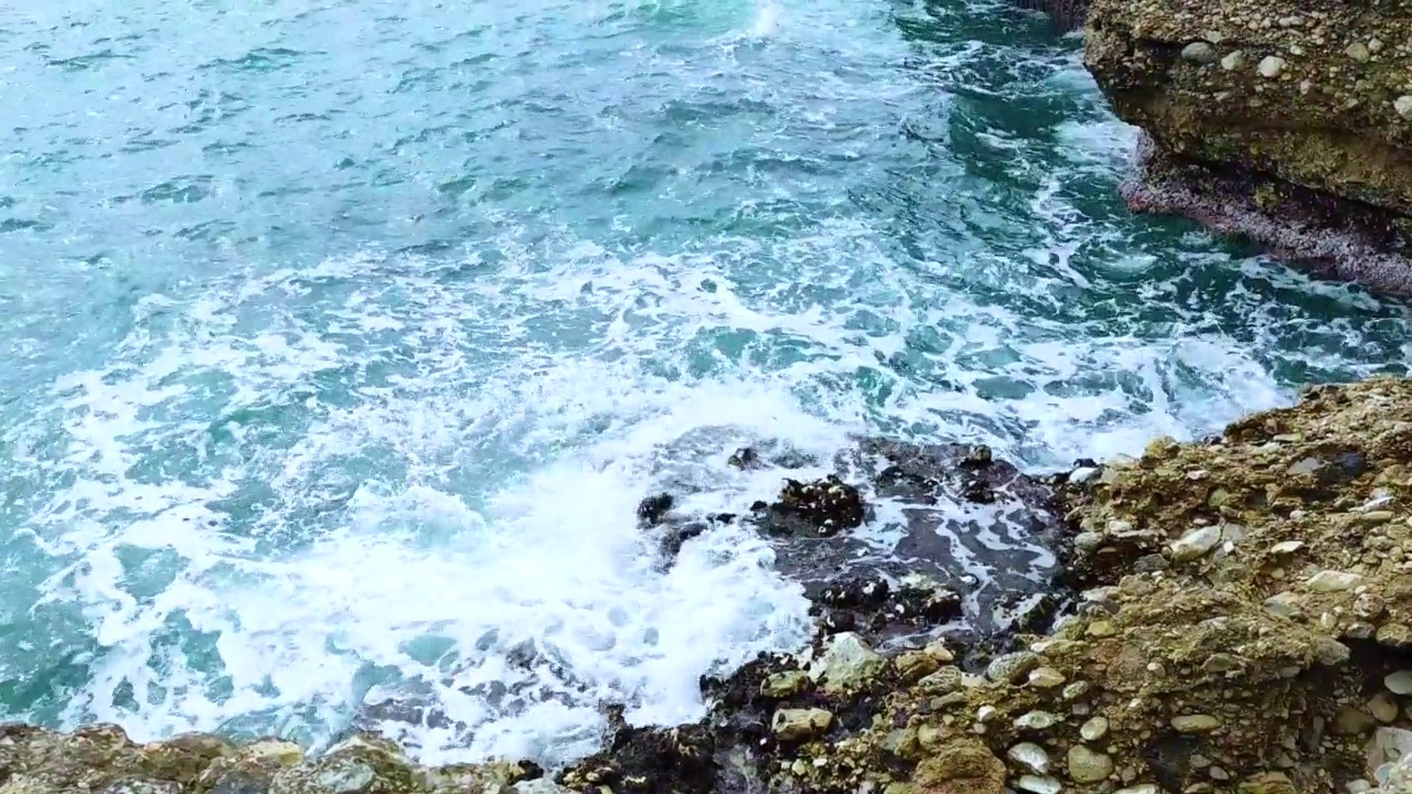 海浪拍打着海岸上的石头。蓝色的大海，淡淡的暴风雨，白色的浪花，晴朗的天气。视频素材