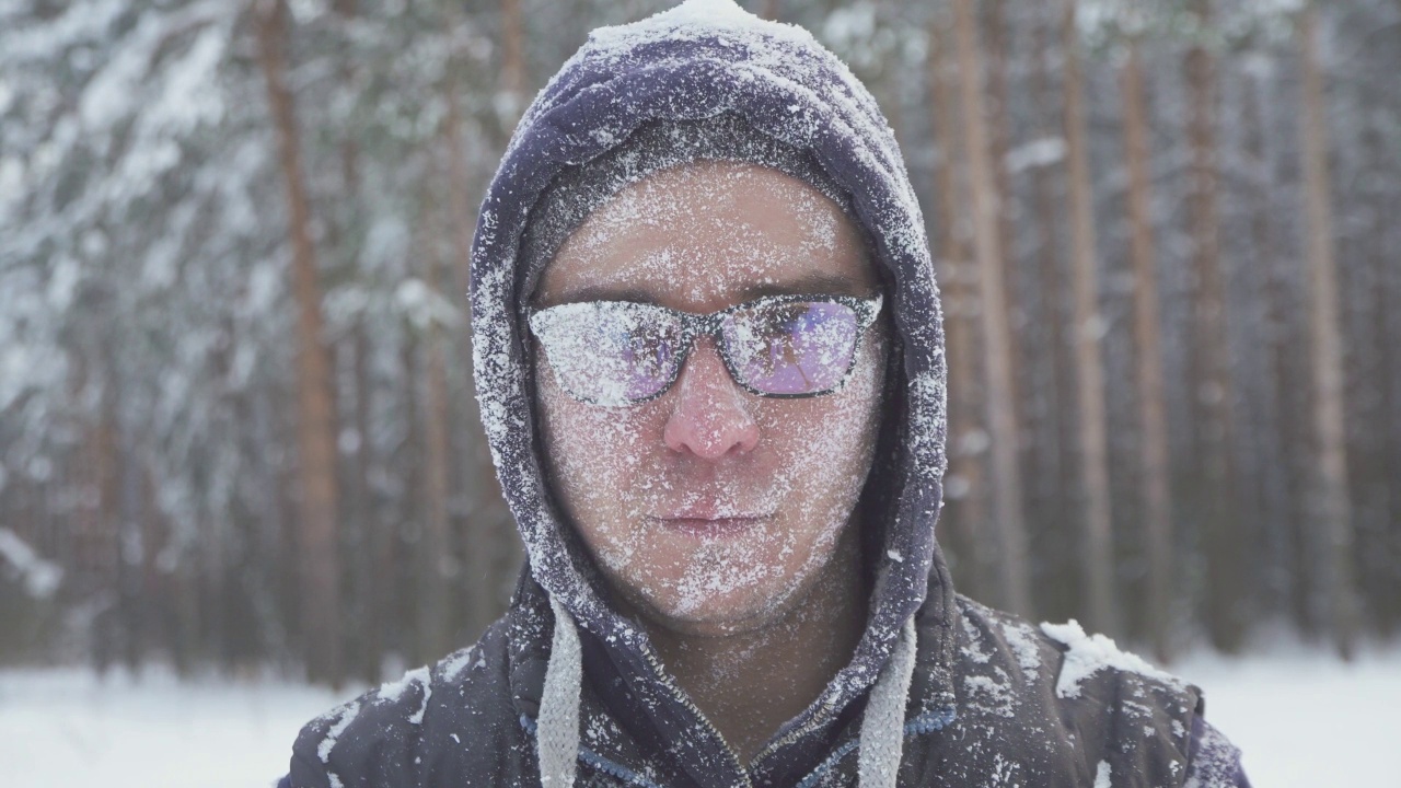 冬天的森林里，一个冰封的戴眼镜的男人，在一场暴风雪后，满脸积雪的他微笑着看着镜头视频素材