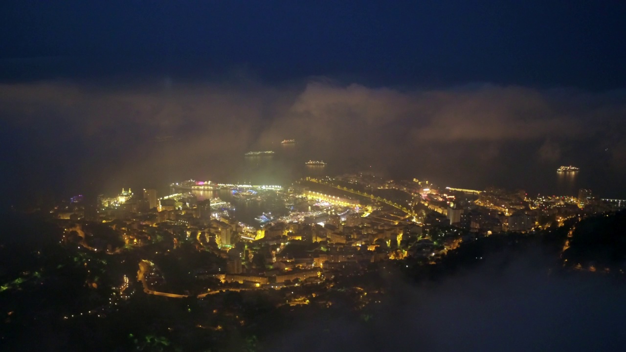 航拍美丽的景色，夜晚有港湾的城市灯火通明，无人机在天空的云层上飞行-摩纳哥视频素材