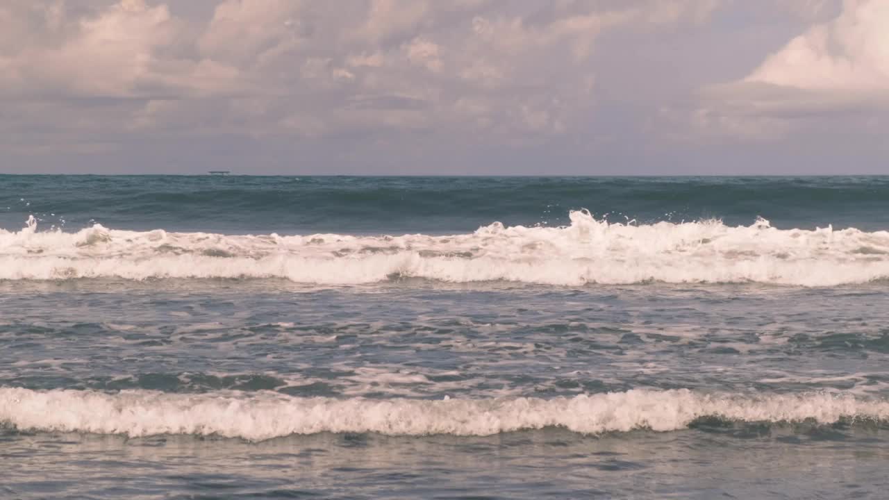 在一个阳光明媚的日子里，巨大的蓝色海浪在印度尼西亚巴厘岛的海岸卷起成一个管状。印度洋上的海浪。波浪泡沫和泡沫滑过水面。真正的时间,4 k视频素材