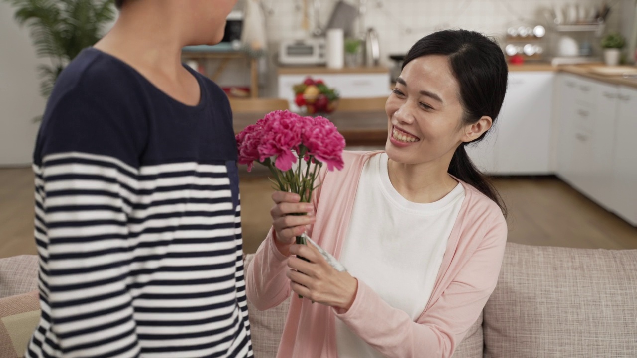 亚洲男孩在家里给妈妈送花的背影。微笑的女人轻抚着儿子的脸，一边闻着花束一边说谢谢视频素材