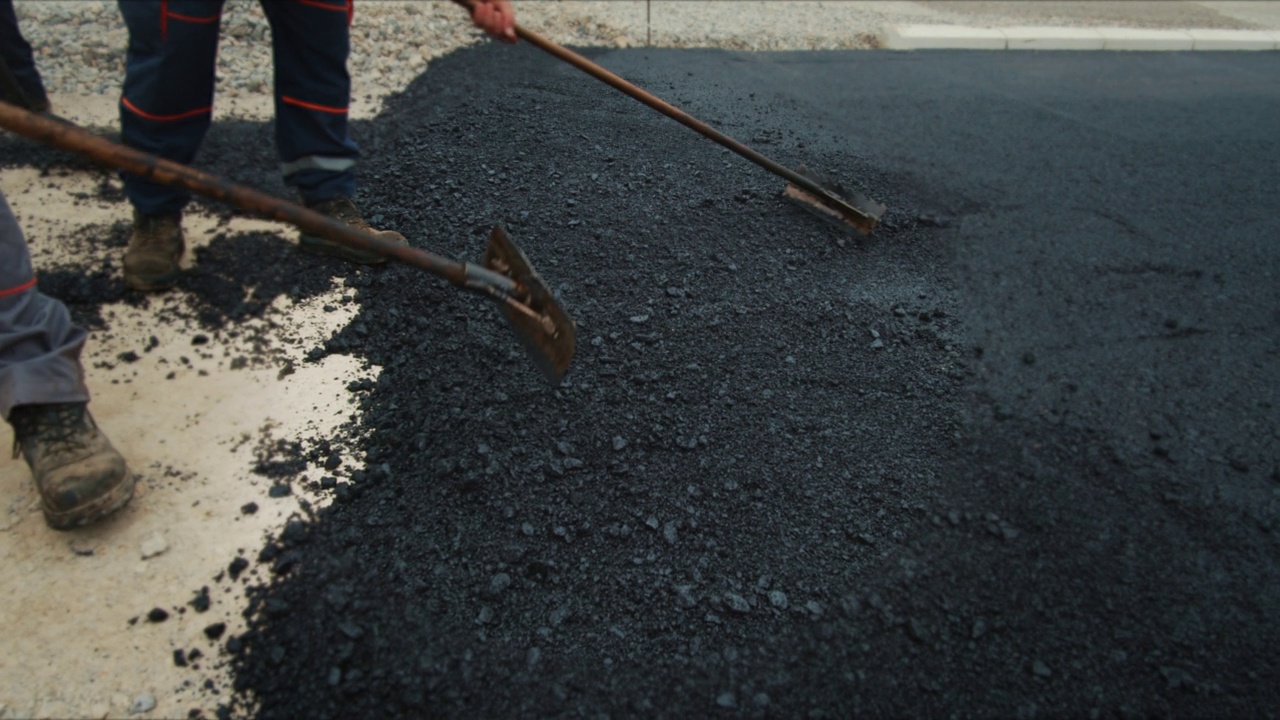 建筑工人正在用耙子沿着公路铺上过热的沥青。给一条新街道铺沥青。股票视频。视频素材