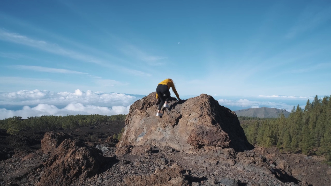 一位年轻的女游客爬上了一块火山石的顶部。在特内里费岛上的泰德火山国家公园，一座高耸入云的山。从观景台上可以看到拉戈梅拉岛和拉帕尔马岛令人难以置信的景色视频素材