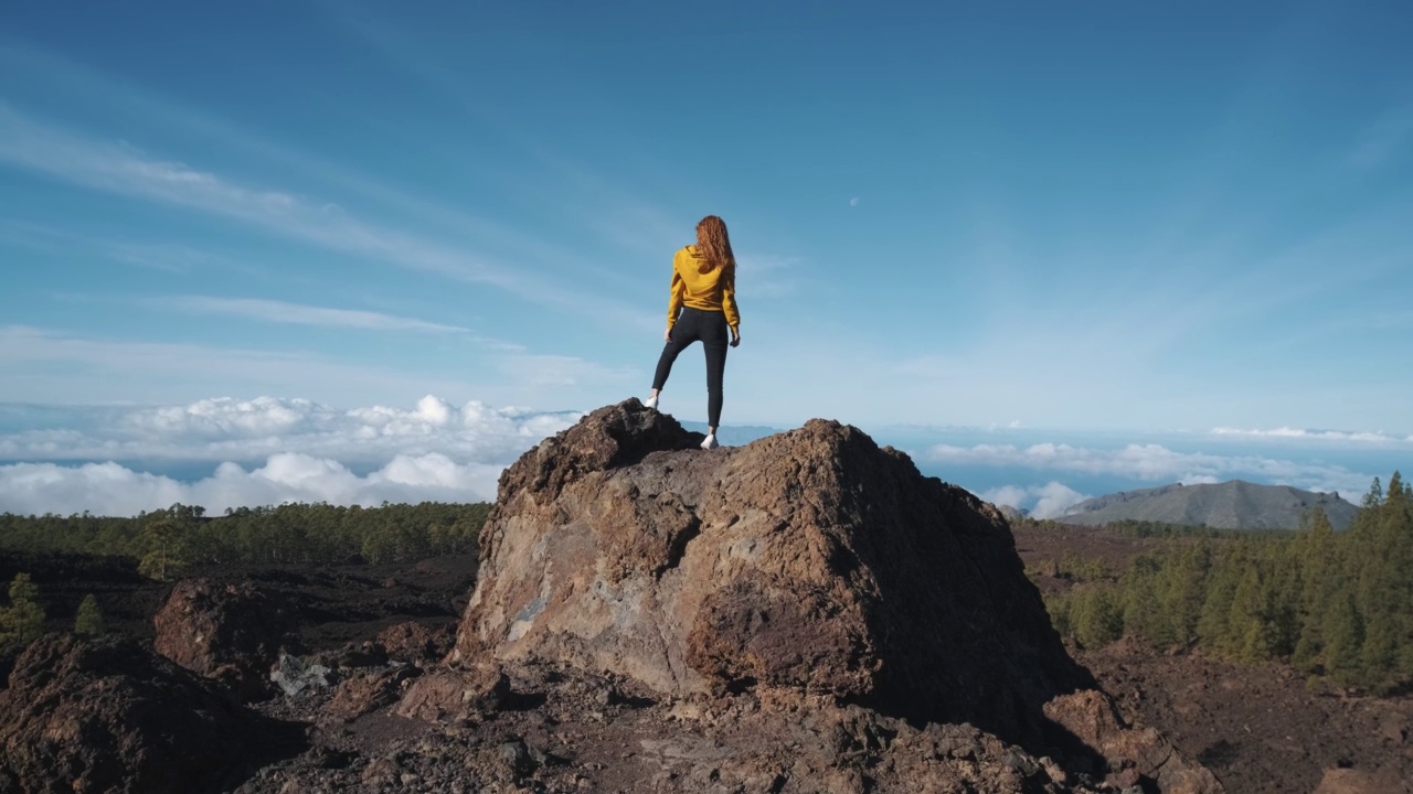 一位年轻的女游客爬上了一块火山石的顶部。在特内里费岛上的泰德火山国家公园，一座高耸入云的山。从观景台上可以看到拉戈梅拉岛和拉帕尔马岛令人难以置信的景色视频素材