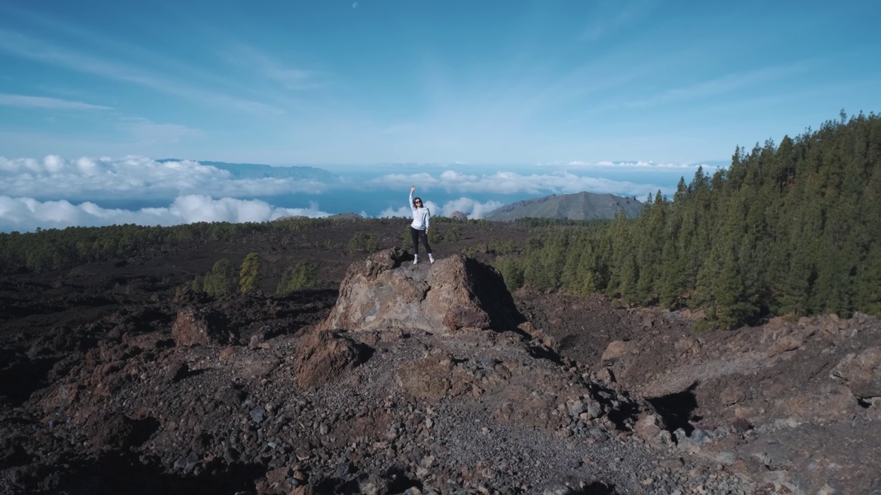 一位年轻的女游客爬上了一块火山石的顶部。在特内里费岛上的泰德火山国家公园，一座高耸入云的山。从观景台上可以看到拉戈梅拉岛和拉帕尔马岛令人难以置信的景色视频素材