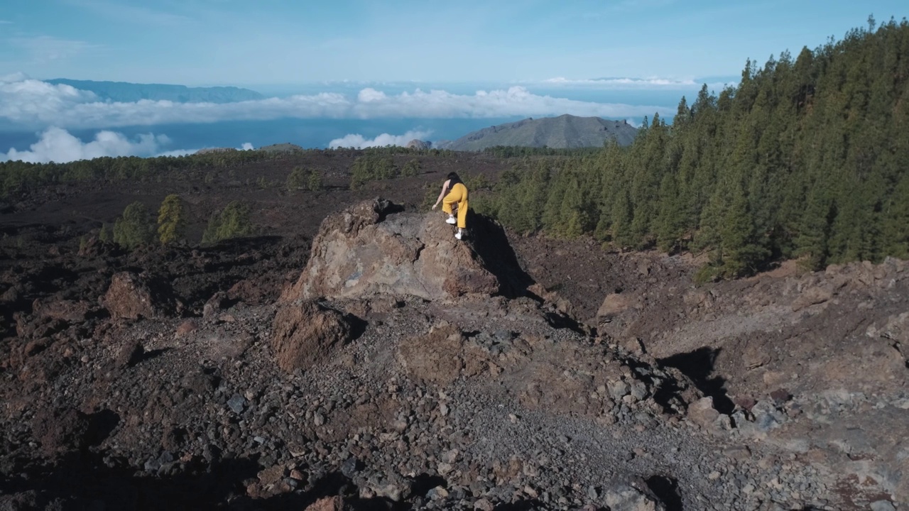 一位年轻的女游客爬上了一块火山石的顶部。在特内里费岛上的泰德火山国家公园，一座高耸入云的山。从观景台上可以看到拉戈梅拉岛和拉帕尔马岛令人难以置信的景色视频素材