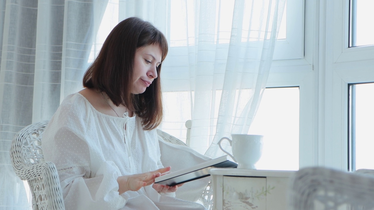 女人坐在靠窗的扶手椅上，读着小说，喝着咖啡或茶视频素材