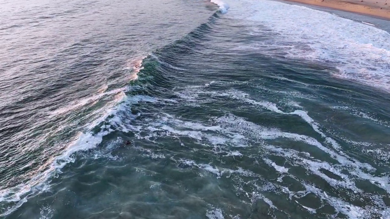 日落时分在埃斯孔迪多港海滩冲浪的鸟瞰图视频素材