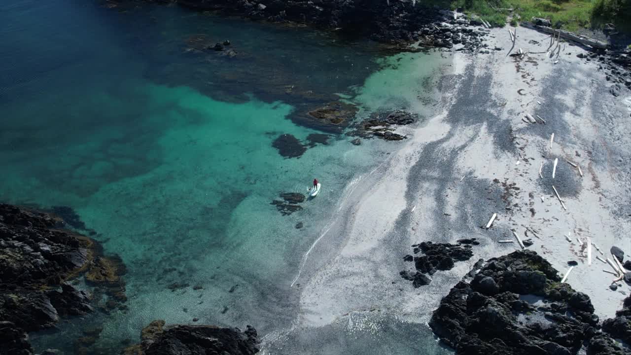 无人机拍摄的一个女人站在一个靠近岛屿和山脉的海湾里划船视频素材