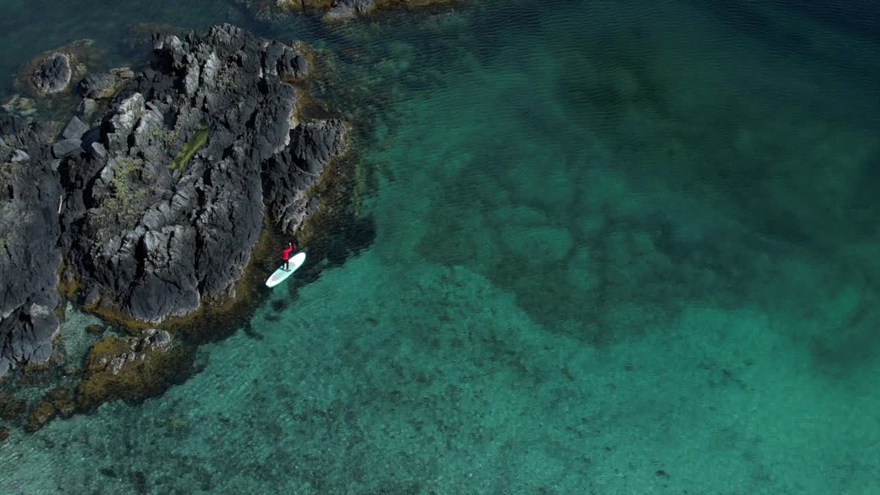 无人机拍摄的一个女人站在一个靠近岛屿和山脉的海湾里划船视频素材