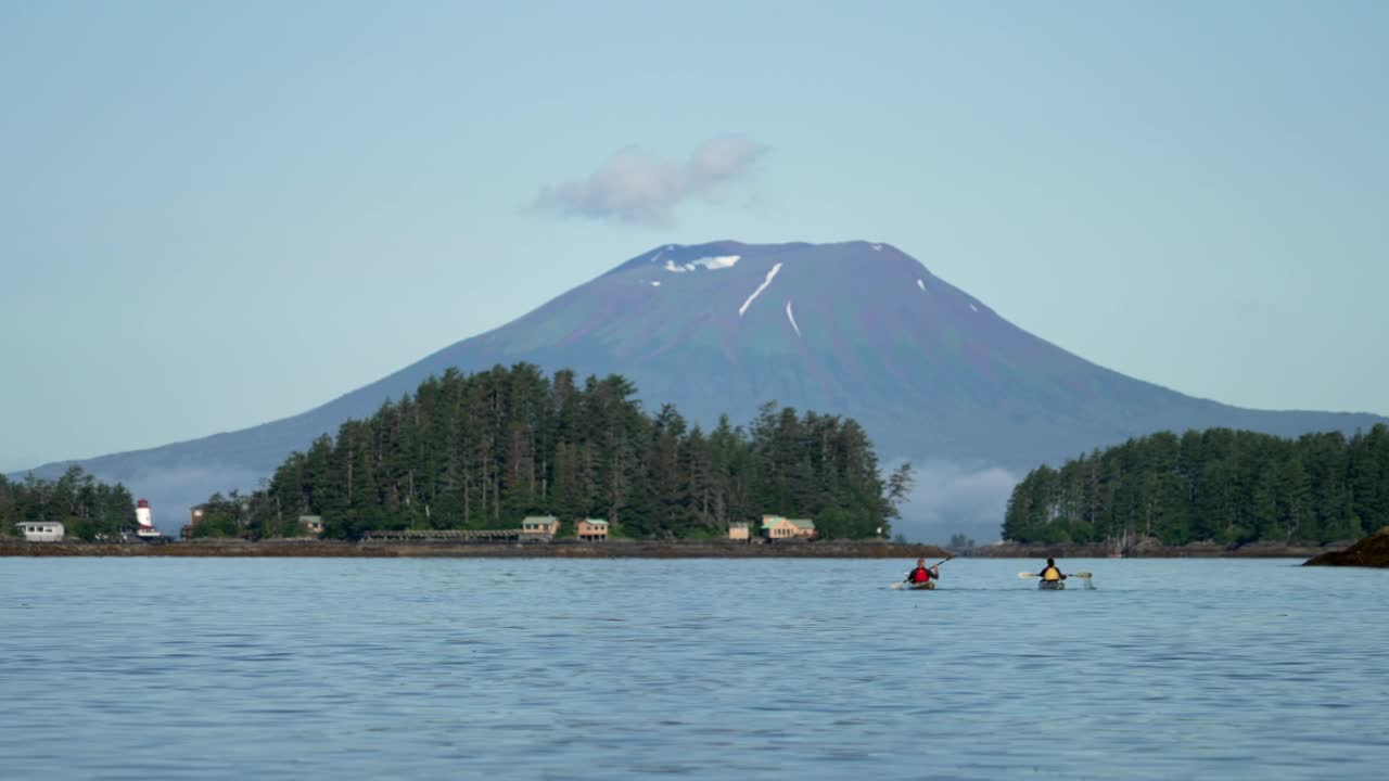 两个年老的皮划艇手在河上划着船，后面是火山视频素材