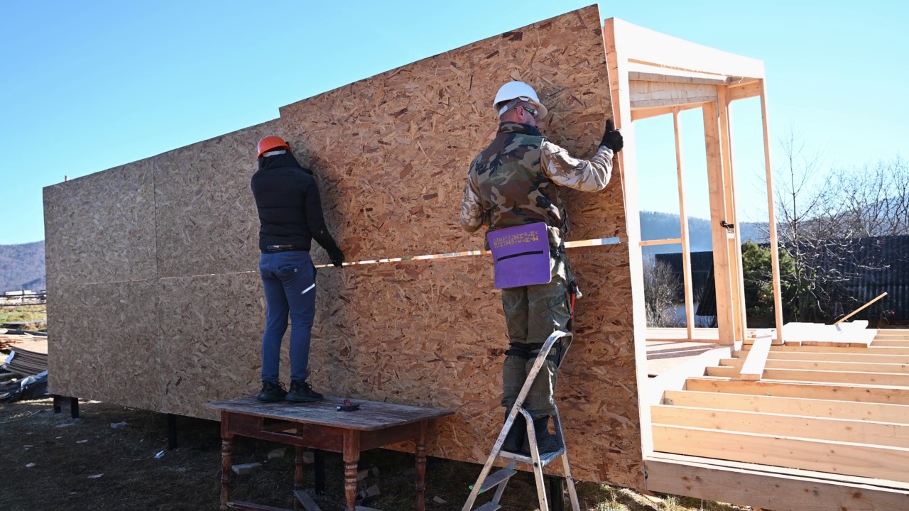 工人正在建造木制框架房屋，安装木质OSB板。视频素材