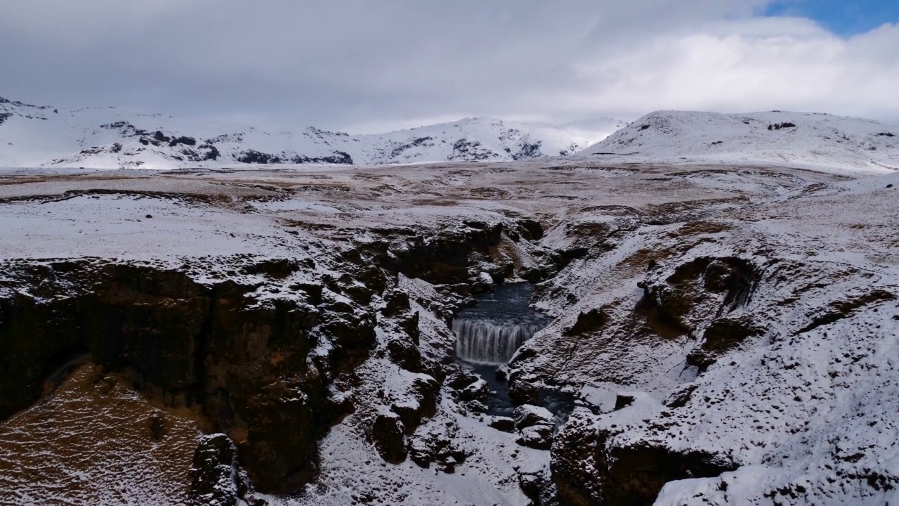 冬天，在Fimmvörðuháls trail附近的岩石峡谷中，有积雪覆盖的草地和崎岖的山脉，冰岛南部，Skógá河的Steinbogafoss瀑布。视频素材