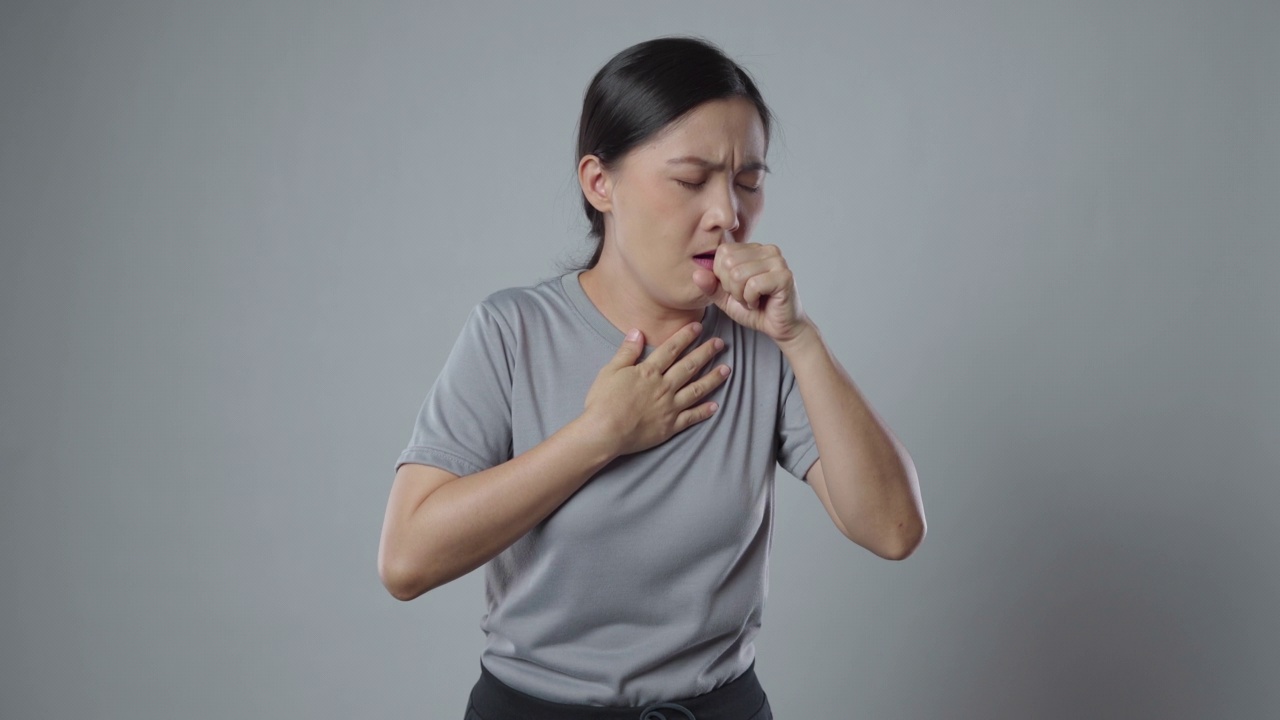 一名亚洲妇女喉咙痛，孤立地站在灰色背景上。视频素材